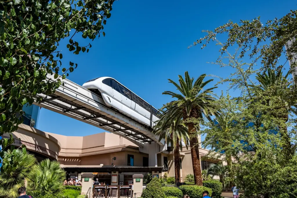 A Las Vegas Monorail train passing above palm trees near MGM Grand