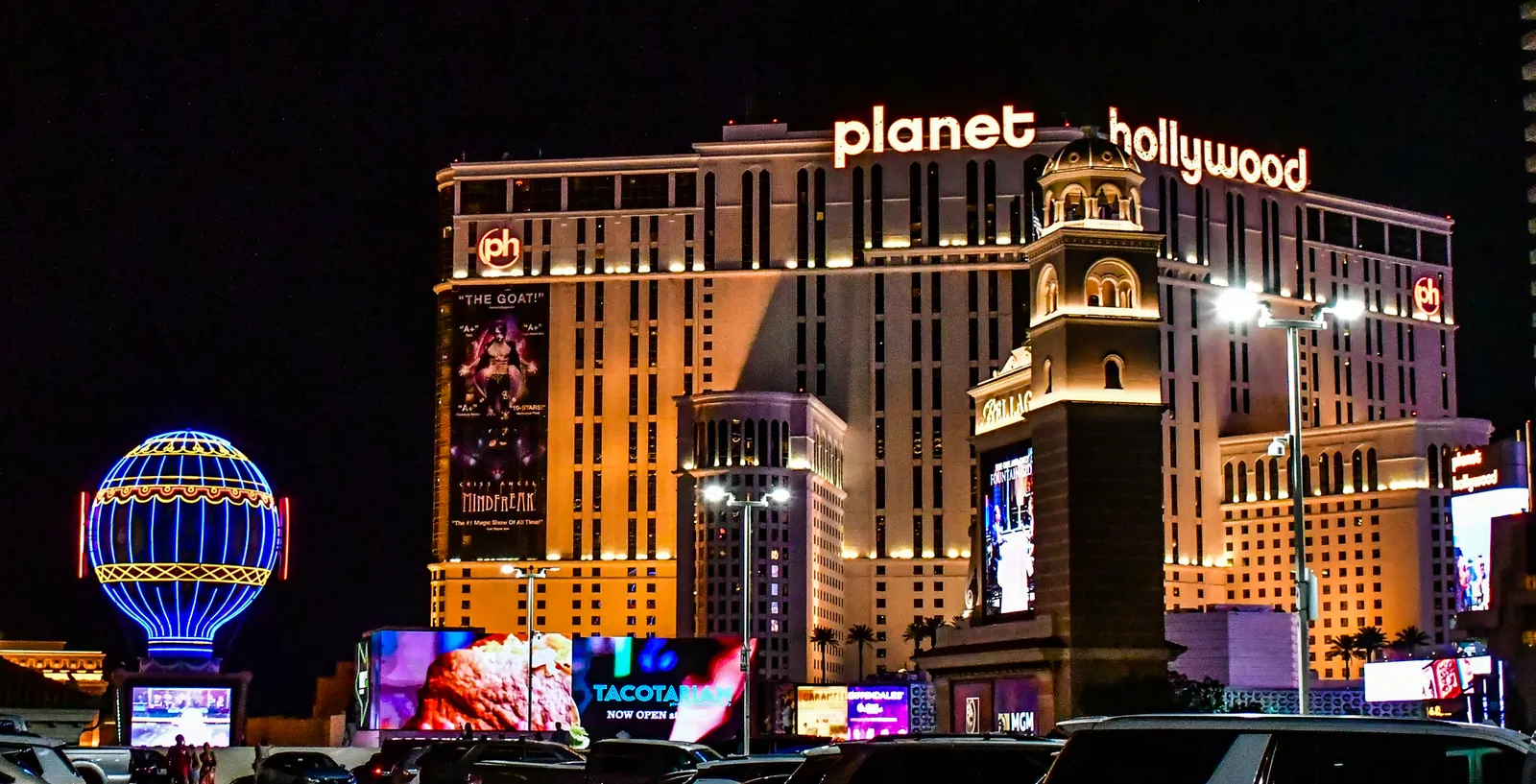 Planet Hollywood Las Vegas lit up at night on the Strip, with the Paris Las Vegas balloon sign at left